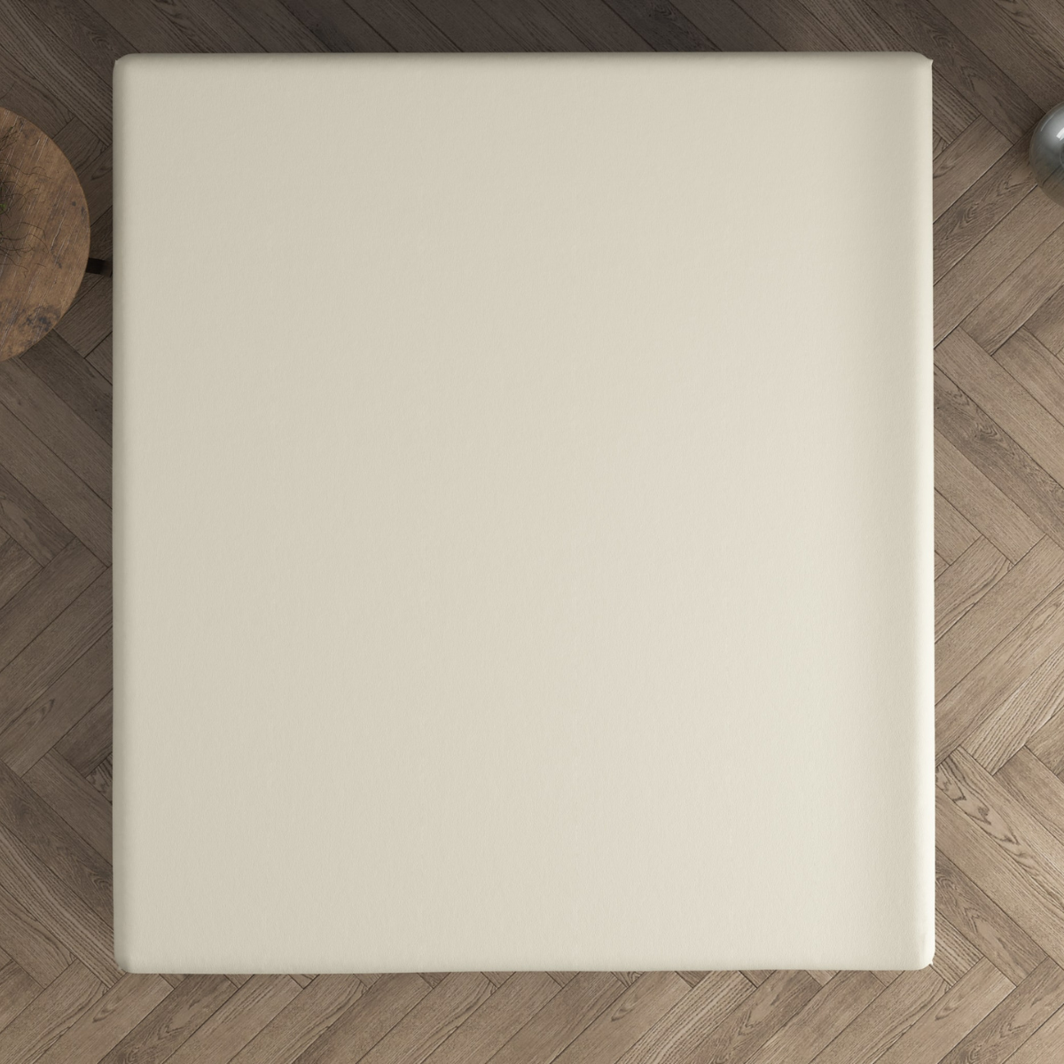 Draufsicht auf eine beigefarbene, quadratische Dreamhouse-Matratze auf einem Holzboden mit Fischgrätenmuster, mit einem runden Tisch auf der linken Seite. Perfekt kombiniert mit dem Doppel Jersey Topper Spannbettlaken - Creme für zusätzlichen Komfort.