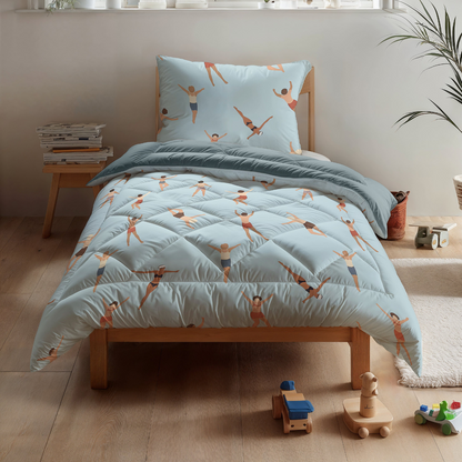 Ein Zelesta Kiddybed Baumwolle - Swimmers mit hypoallergenem Bettzeug und Schwimmeraufdrucken steht neben Holzspielzeug auf einem hellen Boden in einem hellen Zimmer.