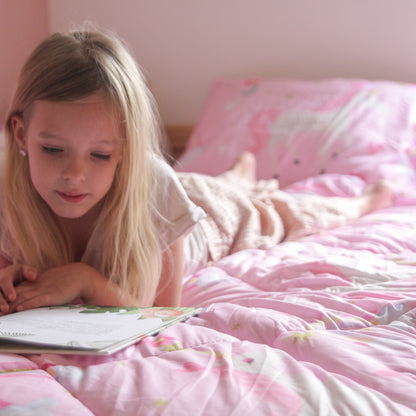 Ein junges Mädchen mit langen blonden Haaren liegt auf dem Bauch in einem Zelesta Kiddybed - Rainbow Unicorn Bett und liest ein aufgeschlagenes Buch.