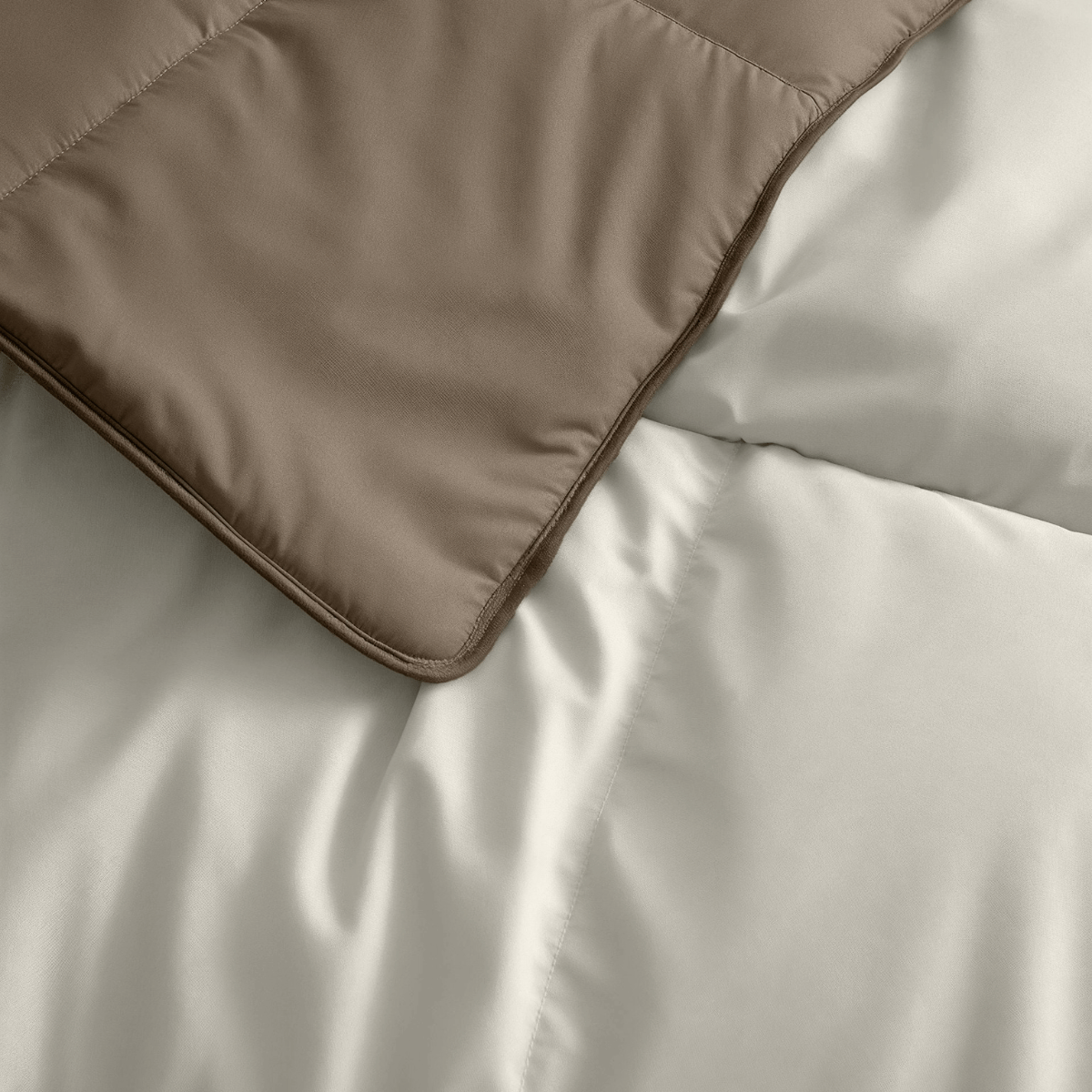 Nahaufnahme des Zelesta Premiumbed Baumwolle - Taupe & Cream, das eine weiße Bettdecke teilweise überlappt. Beide sind mit einem Steppmuster aus unserer luxuriösen Bettdeckenkollektion versehen.