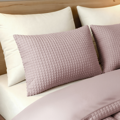 Ein ordentlich gemachtes Bett mit zwei weißen Kissen und einem Zelesta Teddy Check Kissenbezüge - Old Pink Kissen in 80x80cm, zugedeckt mit einer hellrosa superweiche Mikrofaser Bettdecke, steht vor einem hölzernen Kopfteil.