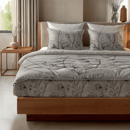 In einem hellen Schlafzimmer steht das Zelesta Royalbed - Butterfly Forest, ein Bett mit Holzrahmen und grauer Bettwäsche mit Blumenmuster, zwei Kissen, eine antiallergische Bettdecke und ein Beistelltisch mit einer Vase und neutralem Dekor.