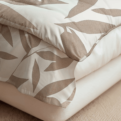 Nahaufnahme einer ordentlich gefalteten Royalbed Baumwolle - Beige Autumn Bettdecke mit einem beige-weißen Blattmuster auf einem schlichten weißen Laken - ideal als allergikergeeignete Bettdecke.