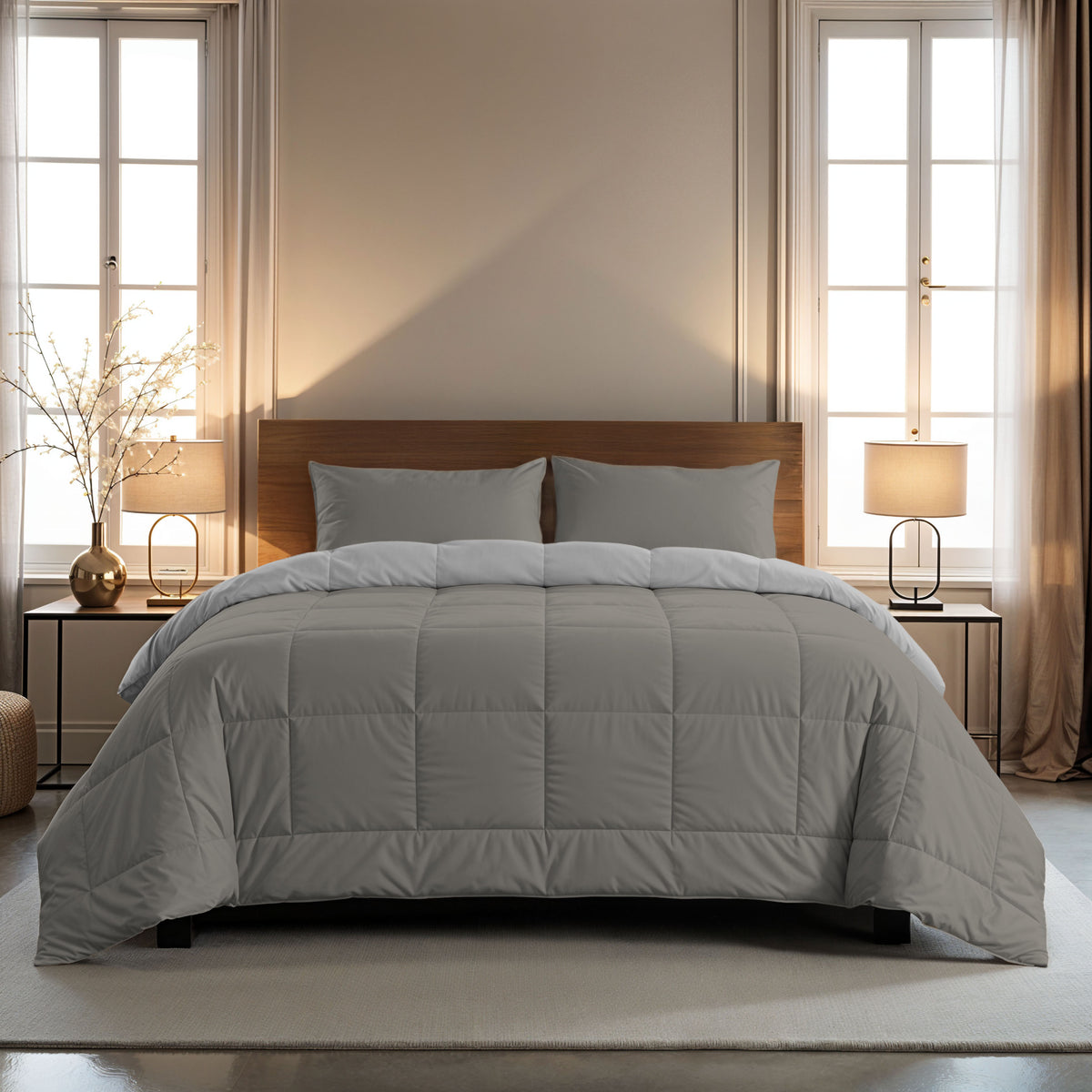 Ein ordentlich gemachtes Bett mit grauen Zelesta Comfort Duo Kissenbezügen Set von 2 (80x80 cm) und einem hölzernen Kopfteil steht in der Mitte zwischen zwei Vorhängen, Beistelltischen und Lampen in einem sanft beleuchteten Schlafzimmer.