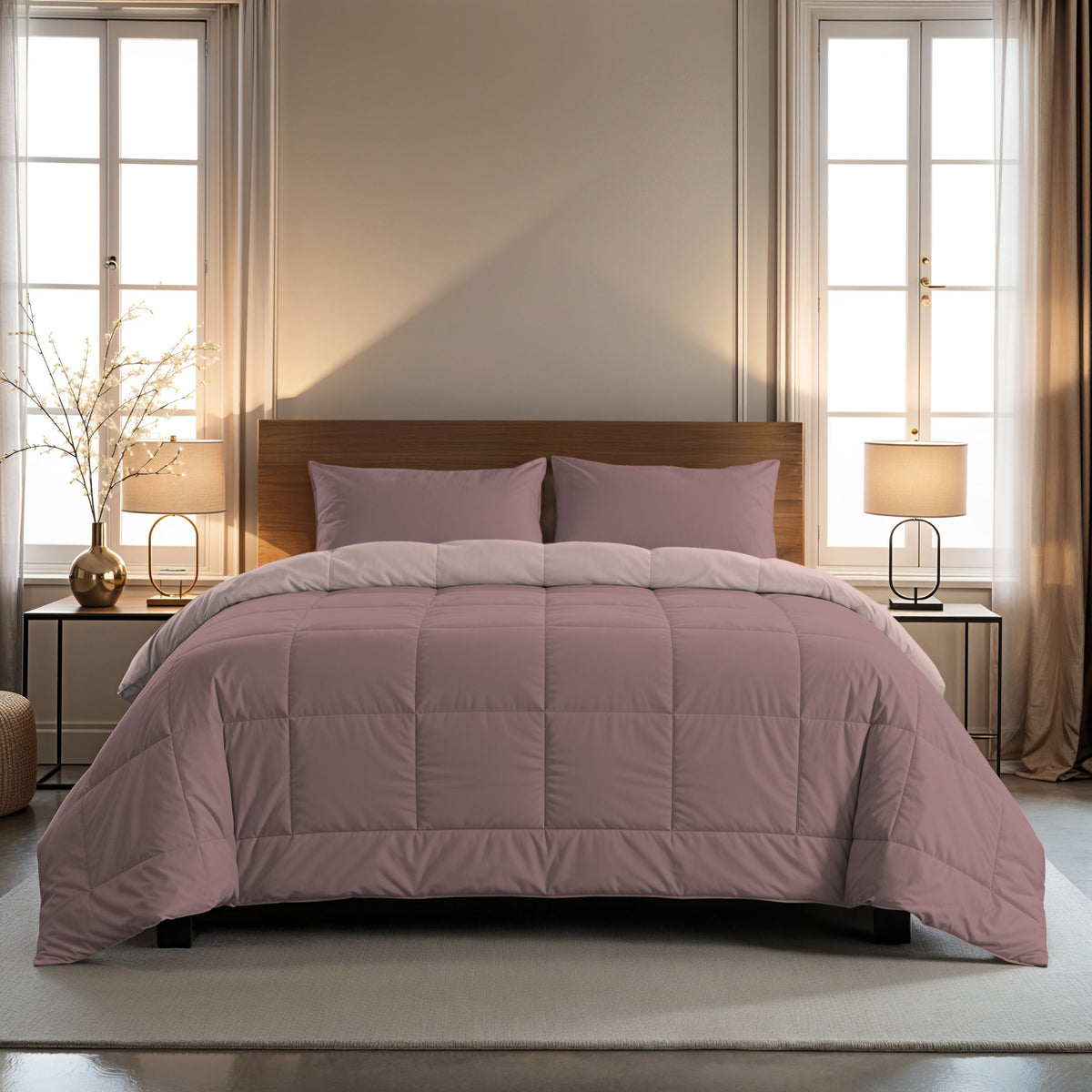 Ein ordentlich gemachtes Bett mit einer lila Bettdecke und zwei 80x80cm Zelesta Comfort Duo Kissenbezügen Set von 2 - Rosa steht zwischen zwei Fenstern, flankiert von Nachttischen und Lampen.