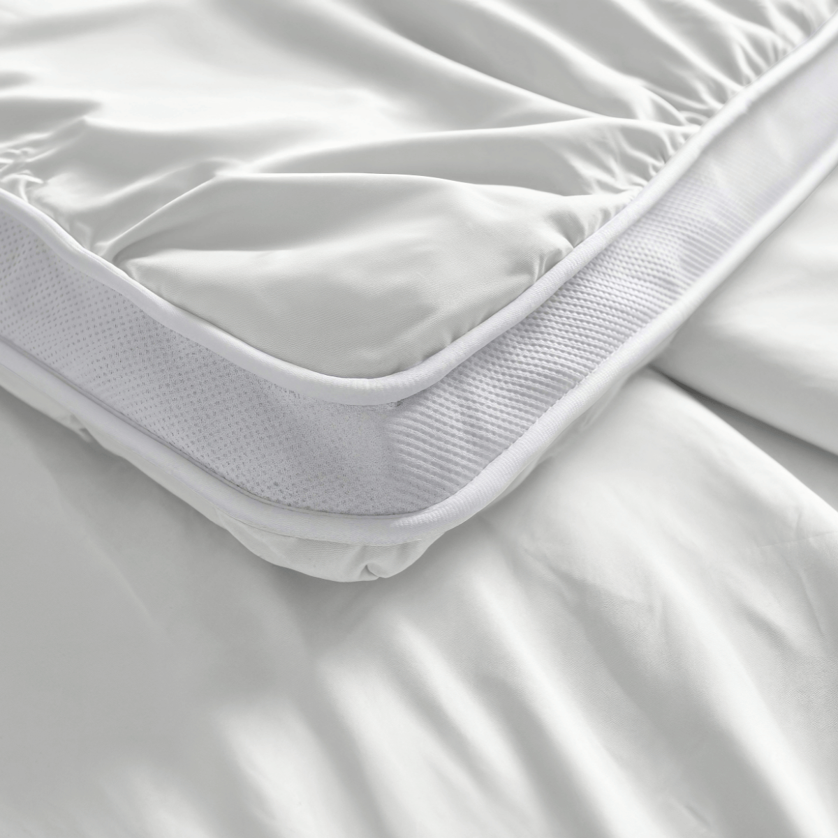 Nahaufnahme des Zelesta Toppers in Weiß mit angepasster Schürze auf einem Bett, mit glattem Stoff, Netzseiten und fortschrittlicher Blue Cell Technology für erhöhten Komfort.