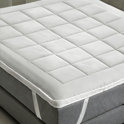Der Zelesta Topper, ein weißer, gesteppter, kühlender Topper mit Ecklaschen, wird auf eine graue Matratze aufgelegt und sorgt für mehr Komfort und ein erfrischendes Schlaferlebnis.