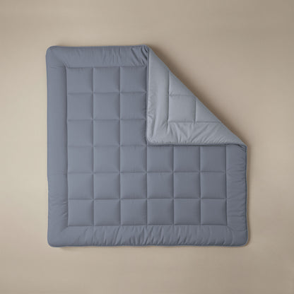 Eine sauber arrangierte, quadratische Zelesta Comfort Duo Bettdecke in Eisblau & Sanftes Blau, bei der eine Ecke gefaltet ist, um die hellere blaue Unterseite zu zeigen, dargestellt auf einem beigen Hintergrund.