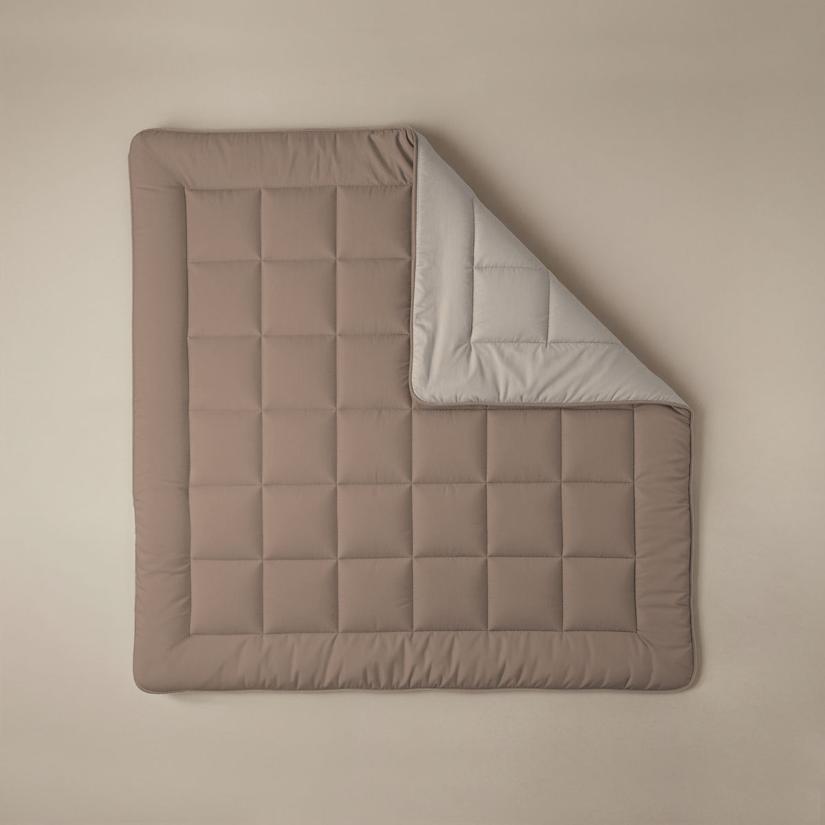 Die Zelesta Comfort Duo Bettdecke - Terra & Sand: Rechteckig, gesteppt, mit festem Bezug, brauner Oberseite und hellgrauer Unterseite. Auf beigem Hintergrund mit umgeschlagener Ecke - ein Klassiker unter den Komfort-Bettdecken.