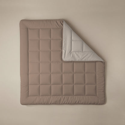 Die Zelesta Comfort Duo Bettdecke - Terra & Sand: Rechteckig, gesteppt, mit festem Bezug, brauner Oberseite und hellgrauer Unterseite. Auf beigem Hintergrund mit umgeschlagener Ecke - ein Klassiker unter den Komfort-Bettdecken.
