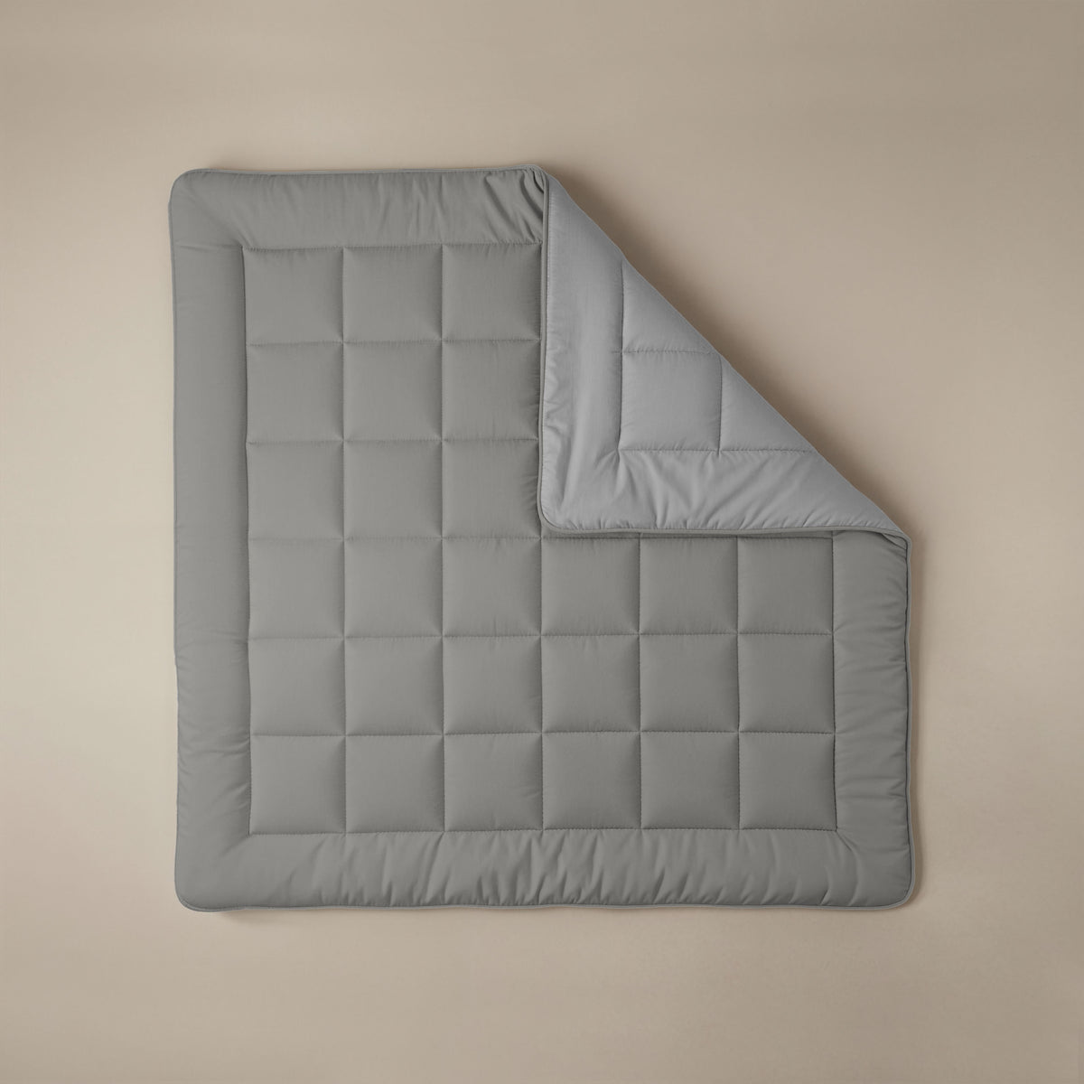 Eine Zelesta Comfort Duo Bettdecke in Grau & Sanftes Grau liegt flach auf einer beigen Fläche, wobei eine Ecke umgeklappt ist, so dass die Unterseite sichtbar wird.