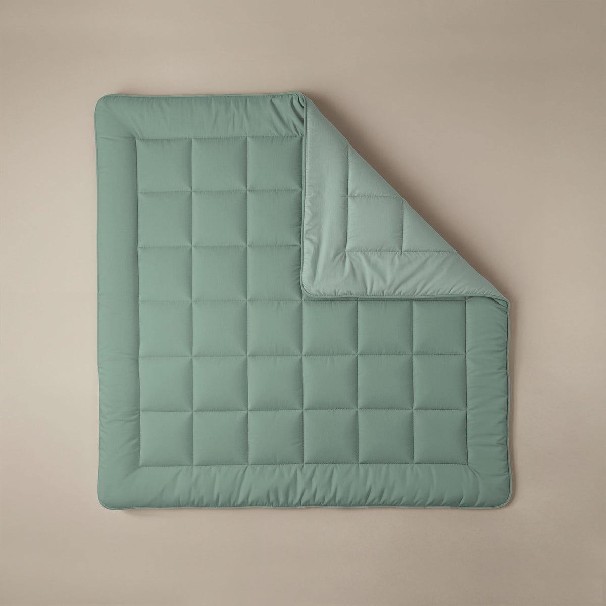 Eine mintgrüne und hellgrüne Zelesta Comfort Duo Bettdecke mit quadratischem Muster liegt flach auf einer beigen Fläche und ist an einer Ecke umgeschlagen.