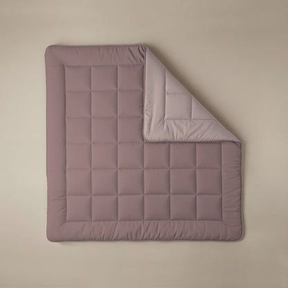 Eine Zelesta Comfort Duo Bettdecke in Rosa & Hellrosa mit einem gesteppten Gittermuster liegt flach auf einer beigen Fläche, eine Ecke ist umgedreht, um die hellere Unterseite zu zeigen.