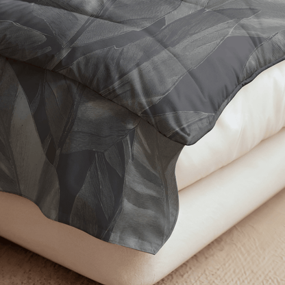 Nahaufnahme eines Bettes mit cremefarbener Matratze und der dunkelgrauen Bettdecke Royalbed Baumwolle - Black Swan mit dezentem Blattmuster, die elegant über den Rand drapiert ist.