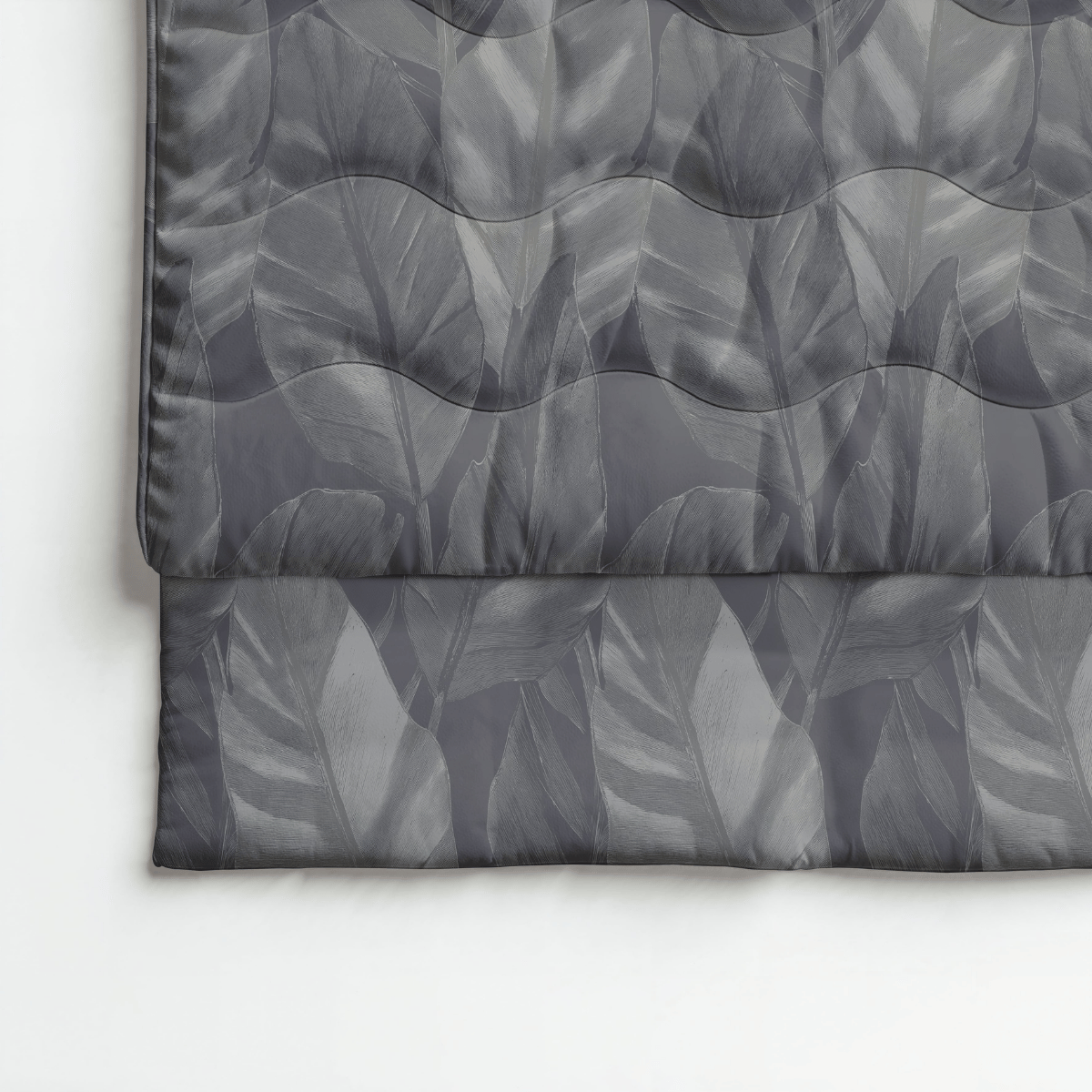 Eine Nahaufnahme der gesteppten Royalbed Baumwolle - Black Swan Bettdecke mit Blattmuster, grauer Farbton, drapiert über einer Bettkante auf einer weißen Fläche - ideal als eine allergikerfreundliche Bettdecke.