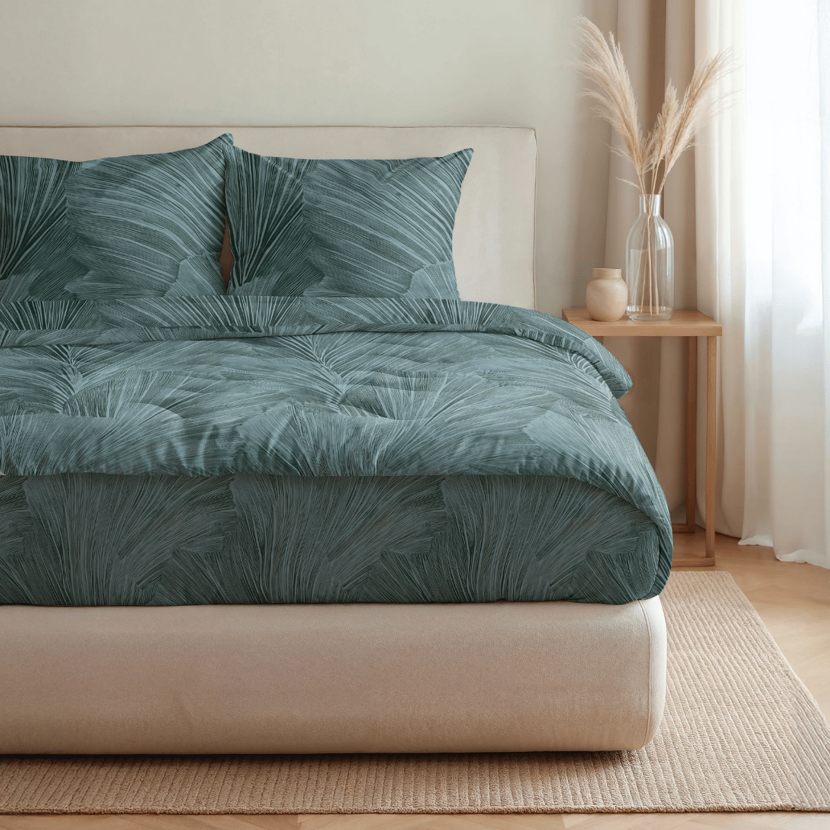 Ein ordentlich gemachtes Bett mit der Royalbed Baumwolle - Botanical Green Bettdecke, zwei Kissen, einem beigen Kopfteil, einem hölzernen Nachttisch und einer Vase mit getrocknetem Pampasgras.