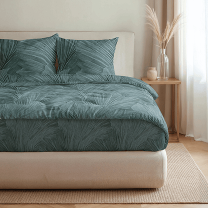 Ein ordentlich gemachtes Bett mit der Royalbed Baumwolle - Botanical Green Bettdecke, zwei Kissen, einem beigen Kopfteil, einem hölzernen Nachttisch und einer Vase mit getrocknetem Pampasgras.