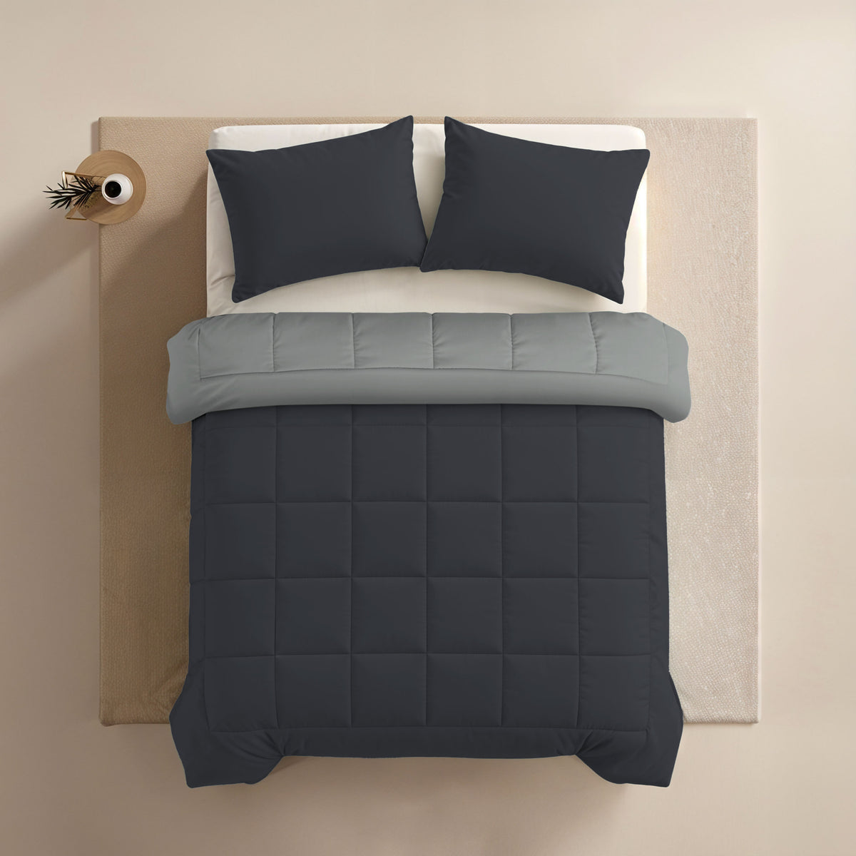 Ein ordentlich gemachtes Bett mit Zelesta Comfort Duo Kissenbezügen Set von 2 - Sanftes Schwarz (80x80cm), einem hellgrauen Oberlaken und einer dunkelgrauen Bettdecke, von oben gesehen auf einem hellen Hintergrund.