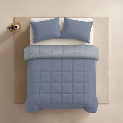 Ein ordentlich gemachtes Bett mit blauen Kissen und der Zelesta Comfort Duo Bettdecke in Eisblau & Sanftes Blau, mit passender blauer Steppdecke, von oben gesehen auf einer beigen Fläche.