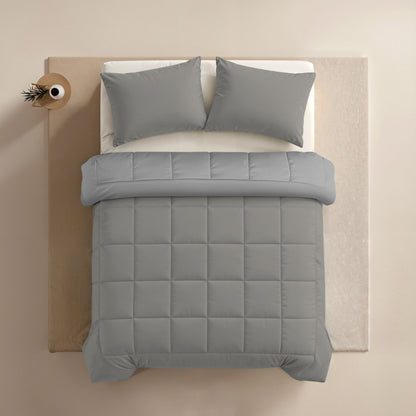 Ein ordentlich gemachtes Bett mit einer Zelesta Comfort Duo Bettdecke in Grau & Sanftes Grau und zwei passenden Kissen, von oben gesehen, neben einem kleinen runden Beistelltisch mit einem Dekorationsartikel.