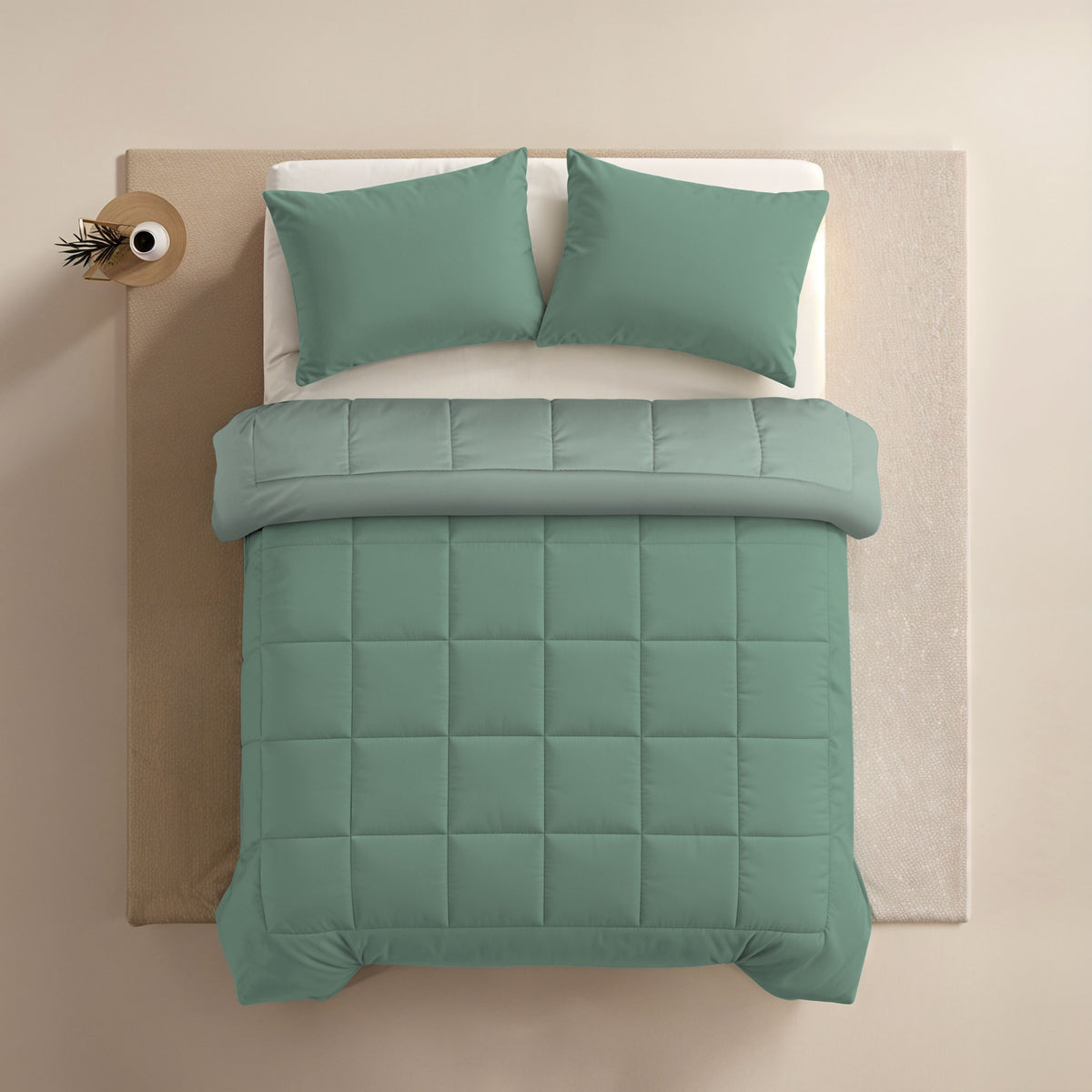 Ein ordentlich gemachtes Bett mit salbeigrünen Kissen und einer Zelesta Comfort Duo Bettdecke in Mintgrün & Hellgrün, von oben gesehen, steht neben einem kleinen runden Beistelltisch mit einem Dekoartikel.