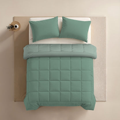 Ein ordentlich gemachtes Bett mit salbeigrünen Kissen und einer Zelesta Comfort Duo Bettdecke in Mintgrün & Hellgrün, von oben gesehen, steht neben einem kleinen runden Beistelltisch mit einem Dekoartikel.