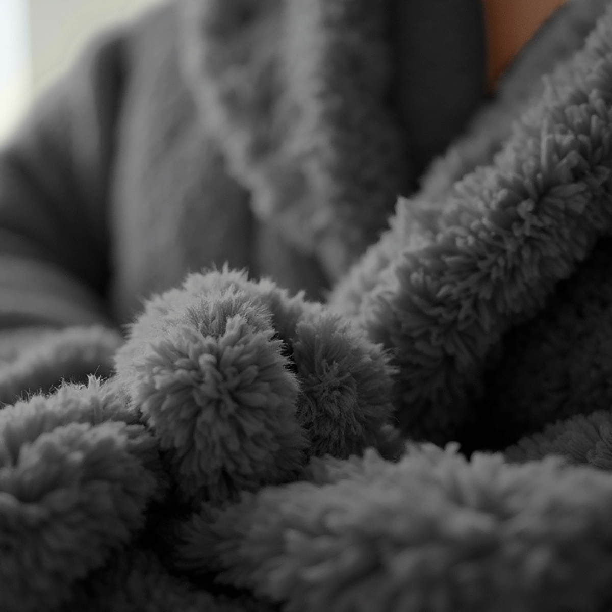 Eine Nahaufnahme der Hand einer Person, die den weichen, strukturierten Stoff des Teddy Morgenmantel Anthrazit in Grau hält, wobei der flauschige und einladende Charakter hervorgehoben wird.
