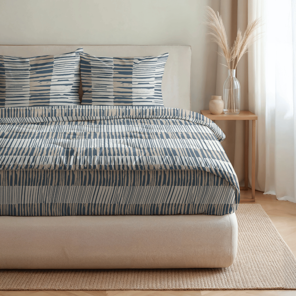 Auf einem ordentlich gemachten Bett mit blau-weiß gestreifter Bettwäsche, zwei passenden Kissen und einem Nachttisch mit Vasen mit getrockneten Gräsern liegt die Royalbed Baumwolle - Checkerboard, eine temperaturregulierende und allergikerfreundliche Bettdecke.