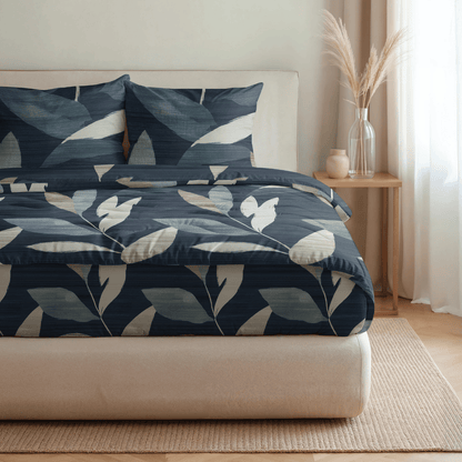 Ein sauber gemachtes Bett mit marineblauer und beiger Bettwäsche mit Blattmuster von Royalbed Baumwolle - Dark Leaves, daneben ein hölzerner Nachttisch mit einer Vase aus Pampasgras und ein Fenster mit Gardinenfilter; ideal für Allergiker.