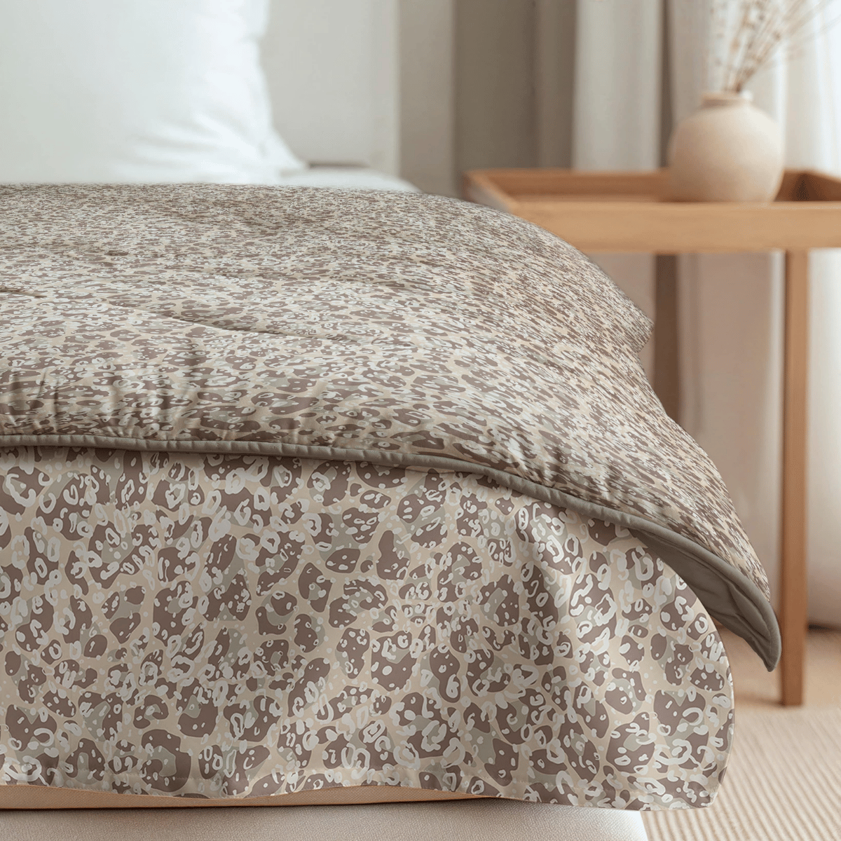 Eine Zelesta Royalbed - Sand Panther Mikrofaser Bettdecke in beige und hellbraunem Muster liegt ordentlich ausgebreitet auf einem Bett neben einem hölzernen Nachttisch mit einer Vase mit Trockenblumen.