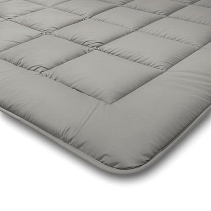 Nahaufnahme einer grauen Zelesta Comfort Duo Bettdecke - Grau & Sanftes Grau Matratzenauflage mit quadratischen Steppnähten und gepolsterten Abschnitten, die in einem Winkel vor einem weißen Hintergrund dargestellt ist.