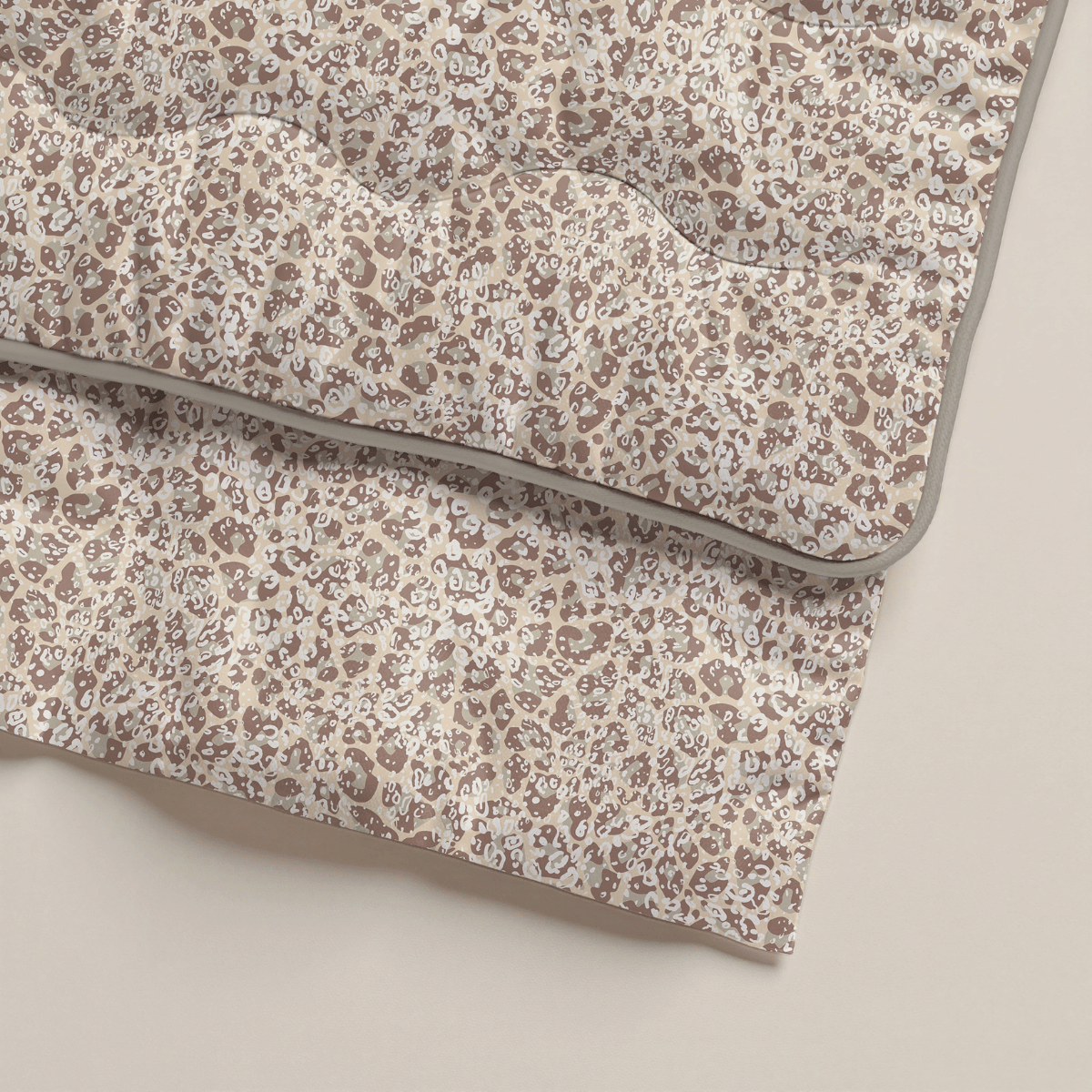 Eine gefaltete Zelesta Royalbed - Sand Panther Mikrofaser Bettdecke mit beigem, braunem und weißem Blumenmuster und grauer Paspel entlang der Ränder wird auf einer hellen Fläche ausgestellt.