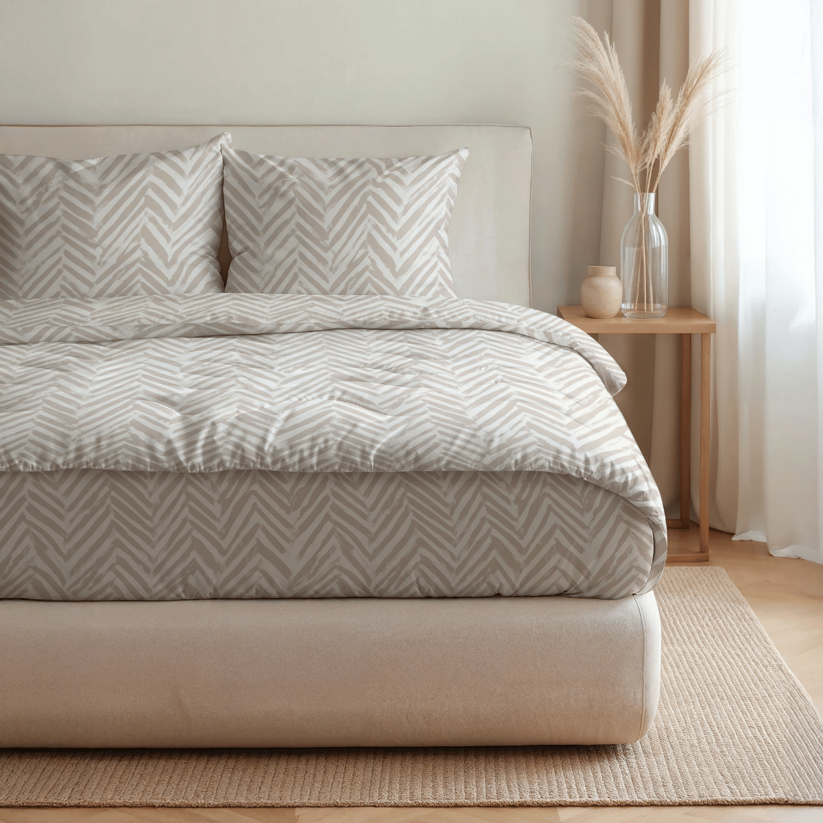 Ein ordentlich gemachtes Bett mit der Royalbed Baumwolle - Ethnic Cream Bettwäsche, zwei Kissen und einem Nachttisch mit einer Vase mit getrocknetem Gras in einem sanft beleuchteten Raum mit neutralem Dekor.