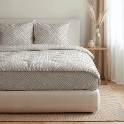 Ein ordentlich gemachtes Bett mit der Royalbed Baumwolle - Ethnic Cream Bettwäsche, zwei Kissen und einem Nachttisch mit einer Vase mit getrocknetem Gras in einem sanft beleuchteten Raum mit neutralem Dekor.