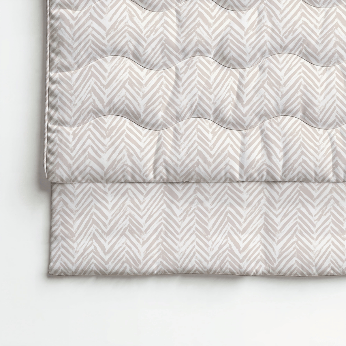 Eine gefaltete beige-weiße Steppdecke mit einem Chevron-Muster, wie die Royalbed Baumwolle - Ethnic Cream, wird auf einer ebenen Fläche ausgelegt.