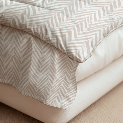 Nahaufnahme eines Bettes mit der Royalbed Baumwolle - Ethnic Cream, einer beige-weiß gemusterten Bettdecke mit temperaturregulierenden und allergikerfreundlichen Eigenschaften, die über ein schlichtes weißes Bettzeug auf einem braunen gepolsterten Lattenrost gelegt wird.