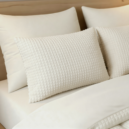 Drei weiße Zelesta Teddy Check Kissenbezüge - Creme (80x80cm, superweiche Mikrofaser) sind ordentlich auf einem Bett mit weißen Laken und einem hellen Holzkopfteil angeordnet.