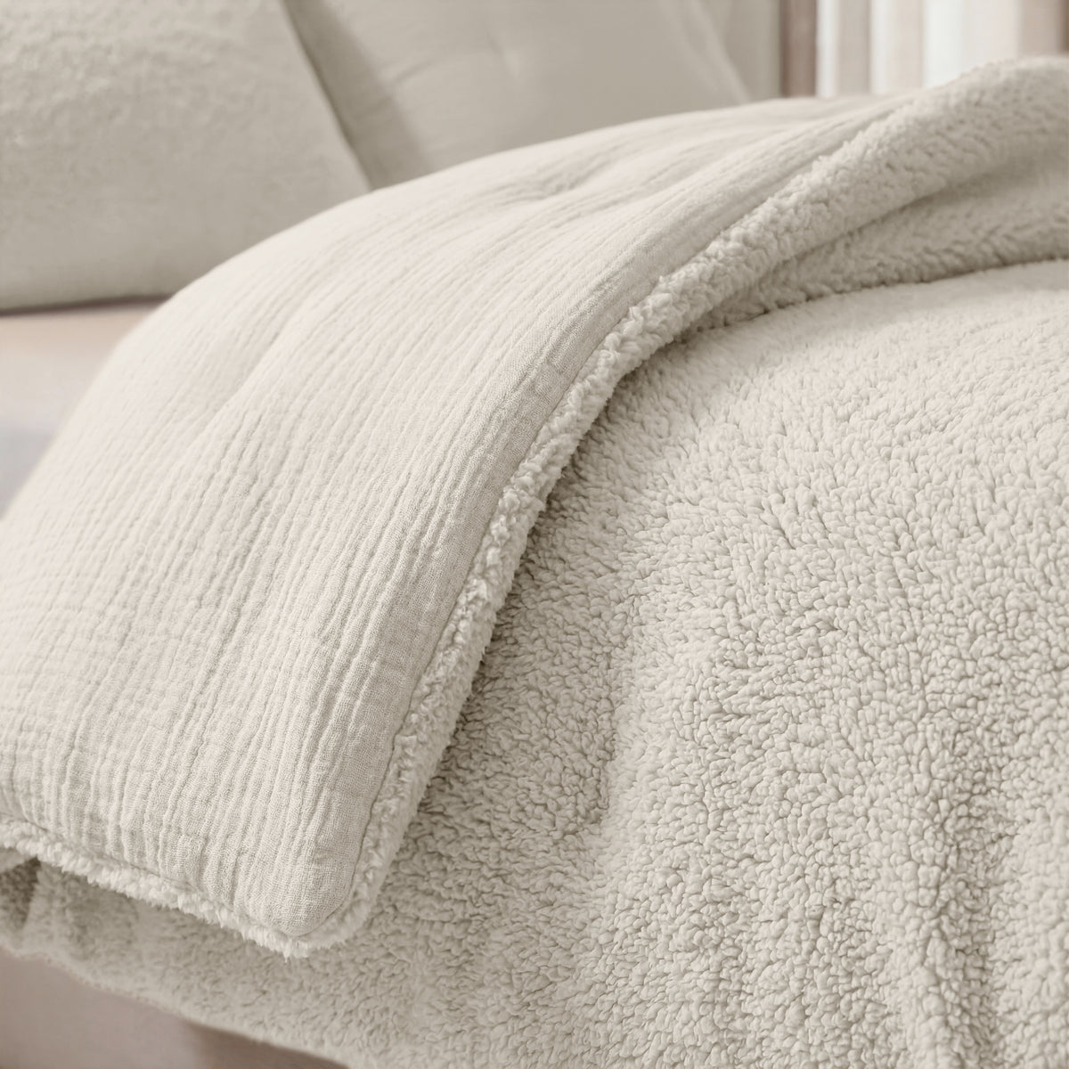 Eine Nahaufnahme eines ordentlich gemachten Bettes mit der Zelesta Teddy Baumwolle Musselin - Beige, einer weichen, flauschigen Steppdecke in hellen Beigetönen.