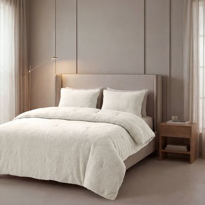 Ein ordentlich gemachtes Bett mit einem beige gepolsterten Kopfteil, Zelesta Teddy Baumwolle Musselin - Beige Bettwäsche und zwei Kissen neben einem hölzernen Nachttisch in einem sanft beleuchteten, neutral getönten Schlafzimmer.