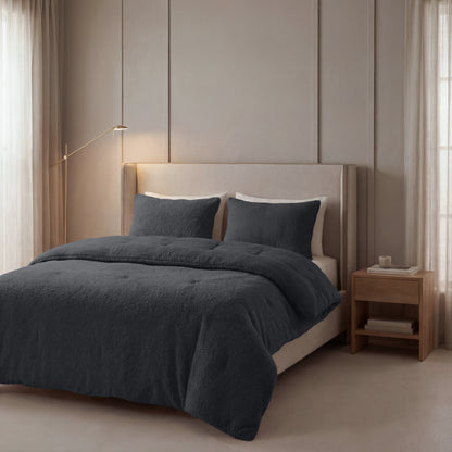 Ein ordentlich gemachtes Bett mit einem beige gepolsterten Kopfteil, dunkelgrauer Bettwäsche, zwei Kissen und dem Zelesta Teddy Baumwolle Musselin - Anthrazit. Nachttisch aus Holz und raumhohe Fenster mit hellen Vorhängen.