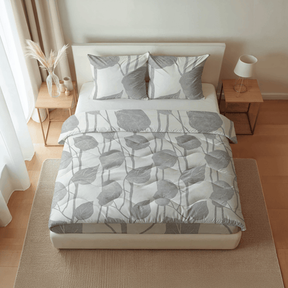 Ein ordentlich gemachtes Bett mit grauer, blattgemusterter Bettwäsche, passenden Kissen und hölzernen Nachttischen ist mit der Royalbed Baumwolle - Spring Buds temperaturregulierenden Bettdecke ausgestattet, die den Komfort in dem sanft beleuchteten Schlafzimmer erhöht.