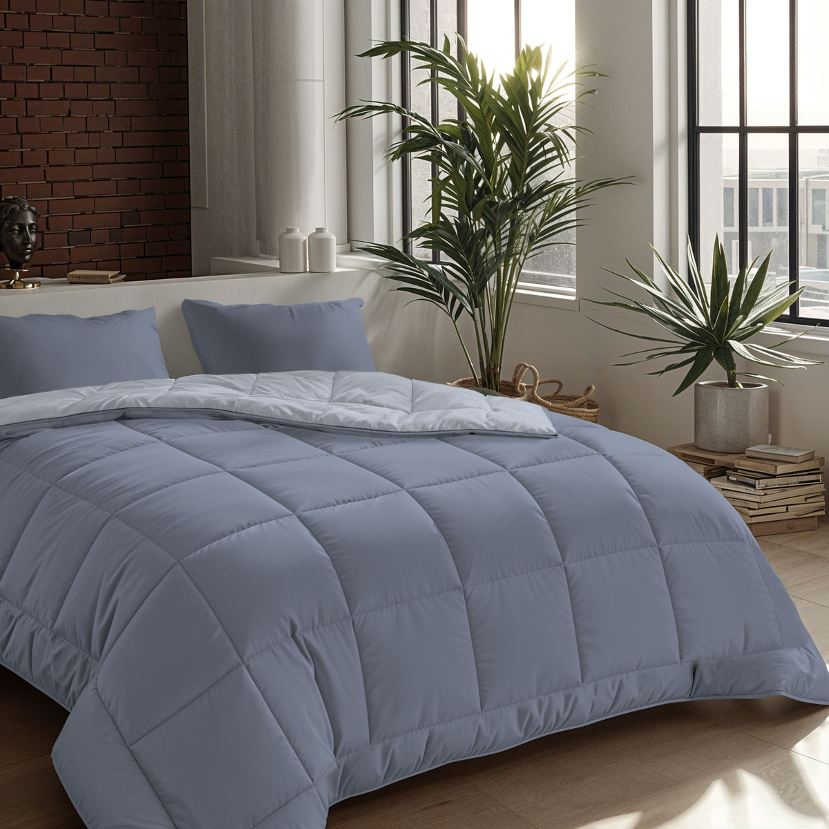 Ein ordentlich gemachtes Bett mit einer Zelesta Comfort Duo Bettdecke in Eisblau & Sanftes Blau und zwei Kissen in einem modernen Schlafzimmer mit großen Fenstern, Topfpflanzen und einer Akzentwand aus Backstein.