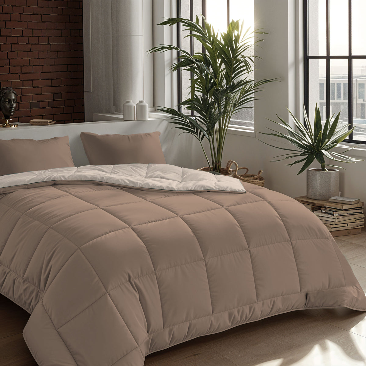 Ein ordentlich gemachtes Bett mit einer beigen Bettdecke und Zelesta Comfort Duo Kissenbezügen Set von 2 - Terra (80x80cm) in einem modernen Schlafzimmer mit großen Fenstern, einer Backsteinwand, Zimmerpflanzen und gestapelten Büchern.