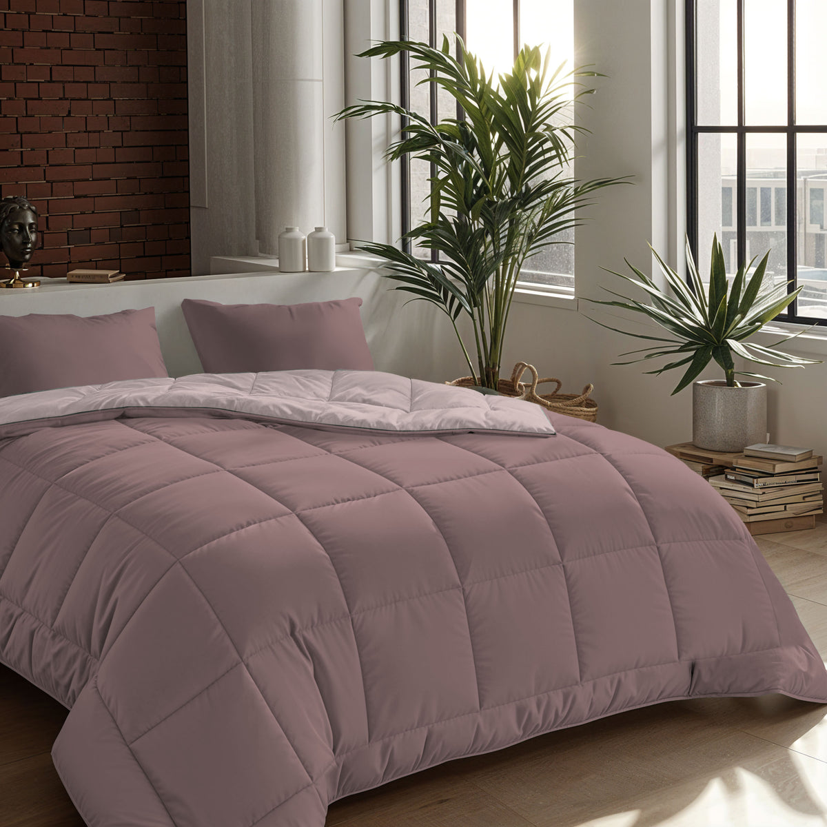 Ein ordentlich gemachtes Bett mit einer lilafarbenen Bettdecke und zwei Zelesta Comfort Duo Kissenbezügen Set von 2 - Rosa (80x80cm) in einem modernen Schlafzimmer mit großen Fenstern, Topfpflanzen und Bücherstapeln auf dem Boden.