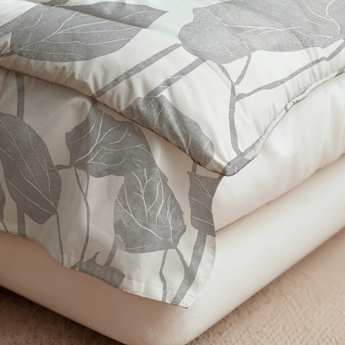 Nahaufnahme eines Bettes mit der Royalbed Baumwolle - Spring Buds, einer cremefarbenen, temperaturregulierenden Bettdecke mit grauem Blattmuster, die über heller Bettwäsche liegt.