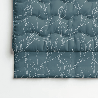 Eine gefaltete Royalbed Baumwolle - White Leaves Bettdecke in dunklem Teal mit einem weißen abstrakten Blattmuster ruht auf einer weißen Oberfläche.