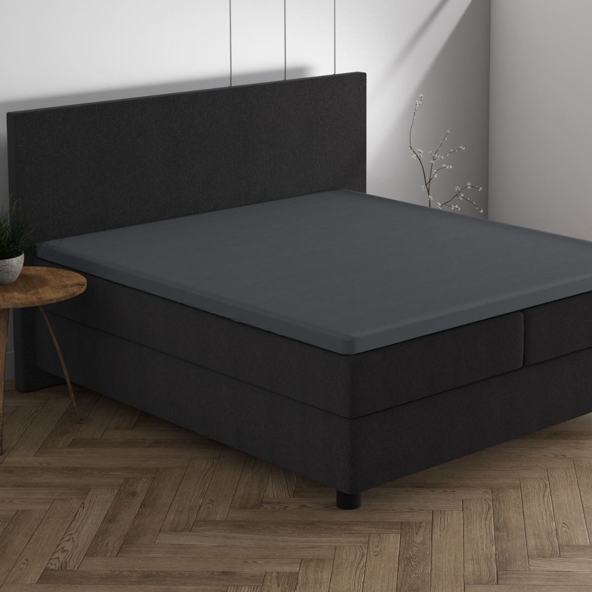 Ein modernes Schlafzimmer mit einem dunklen Polsterbett, dem Doppel Jersey Topper Spannbettlaken in Anthrazit auf der Matratzenauflage, einem Beistelltisch aus Holz, einer Topfpflanze und einem Holzboden im Fischgrätmuster - perfekt für Ihr Traumhaus.