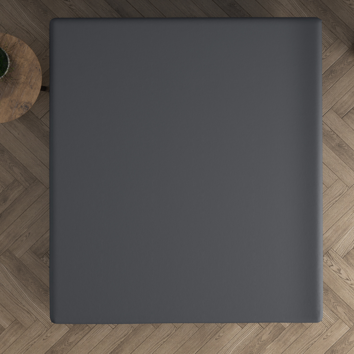 Ein quadratischer schwarzer Tisch, von oben gesehen, auf einem Holzboden mit Fischgrätenmuster, mit einem kleinen runden Beistelltisch aus Holz und einem Topfkaktus in der Nähe - eine gemütliche Dreamhouse-Atmosphäre, ideal zum Entspannen auf dem Doppel Jersey Topper Spannbettlaken - Anthrazit.