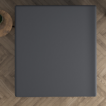 Ein quadratischer schwarzer Tisch, von oben gesehen, auf einem Holzboden mit Fischgrätenmuster, mit einem kleinen runden Beistelltisch aus Holz und einem Topfkaktus in der Nähe - eine gemütliche Dreamhouse-Atmosphäre, ideal zum Entspannen auf dem Doppel Jersey Topper Spannbettlaken - Anthrazit.