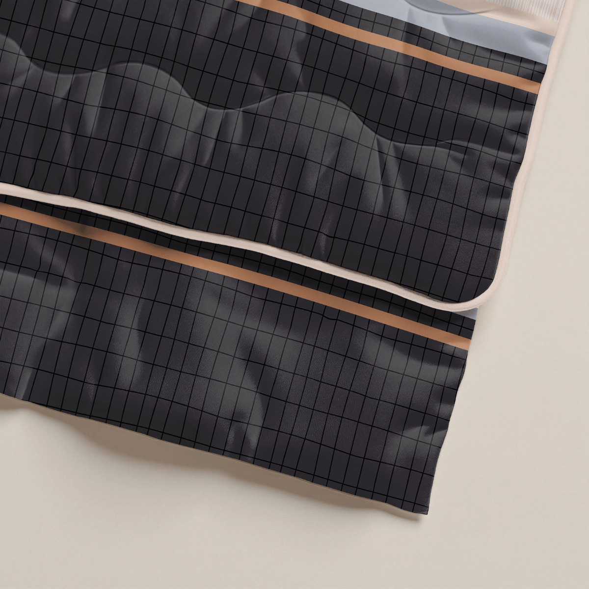 Eine Nahaufnahme des dunklen, gesteppten Stoffes mit Gittermuster und dünnen beigen und braunen Streifen entlang der Ränder, gelegt auf eine helle Oberfläche - ideal als antiallergische Bettdecke wie das Zelesta Royalbed - Blue Stripes.